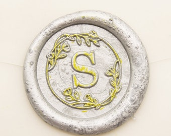 May include: A silver wax seal with a gold floral design and the letter "S" in the centre.
