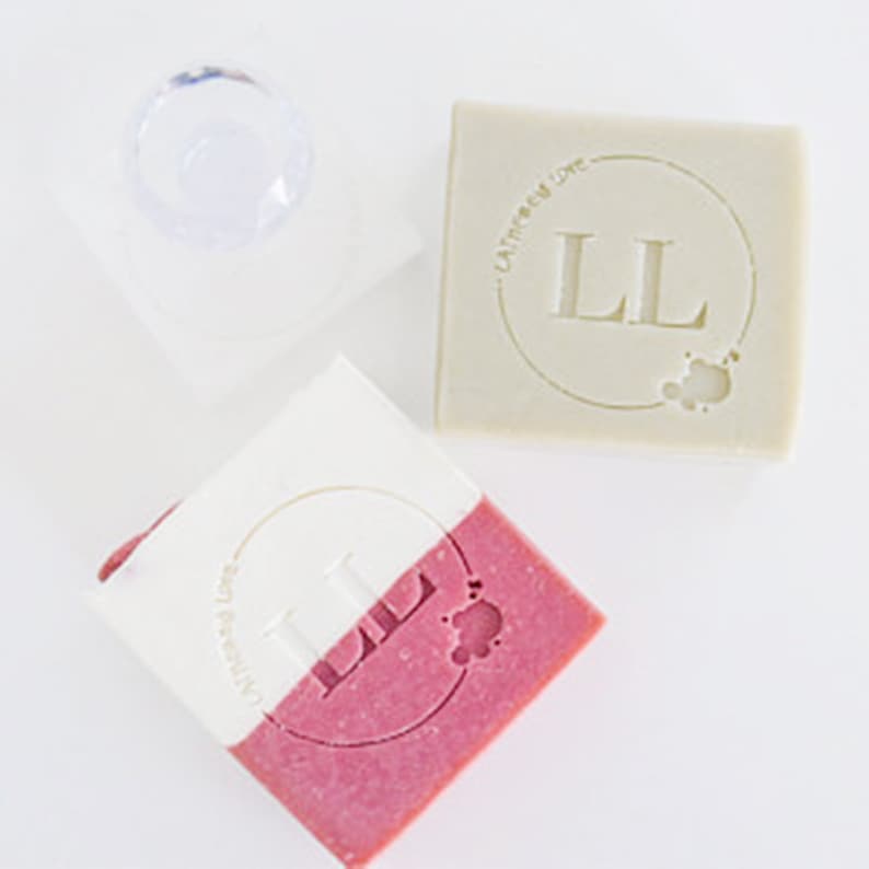 May include: Two bars of soap with the letters "LL" in a circle and the text "Lather & Love" on the top bar. The bottom bar is pink and the top bar is white.