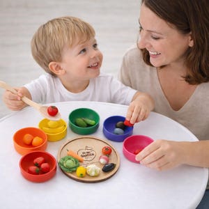 May include: A child and an adult are playing with a wooden toy set. The set includes colourful bowls and wooden vegetables. The child is holding a wooden spoon with a tomato on it. The set is on a white table.