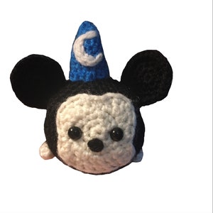 May include: A crocheted plush toy of Mickey Mouse wearing a blue and white wizard hat. The toy has black ears, a white face, and black eyes.