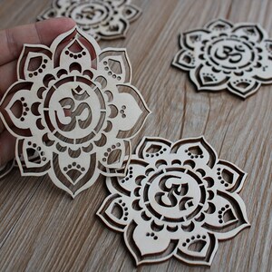 May include: Four wooden laser cut coasters with a mandala design and the Om symbol in the center. The coasters are light brown and have a natural wood finish.