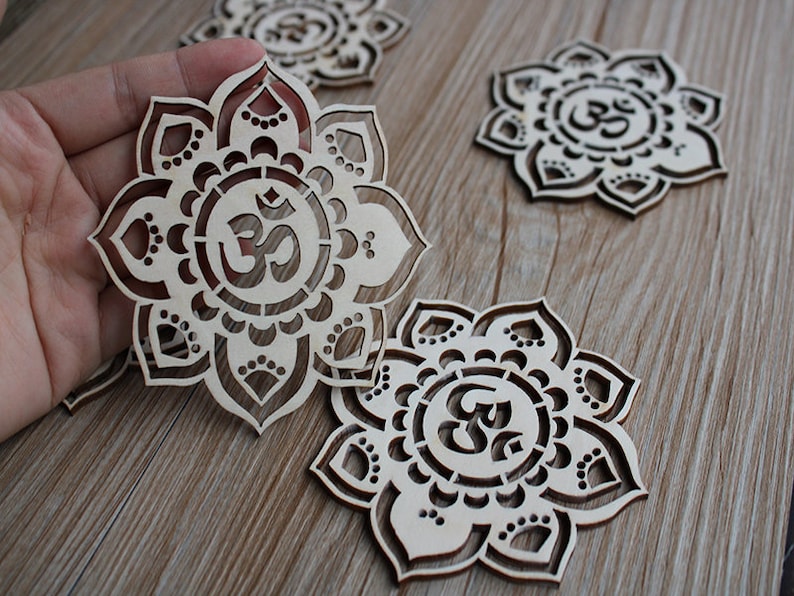 May include: Four wooden laser cut coasters with a mandala design and the Om symbol in the center. The coasters are light brown and have a natural wood finish.