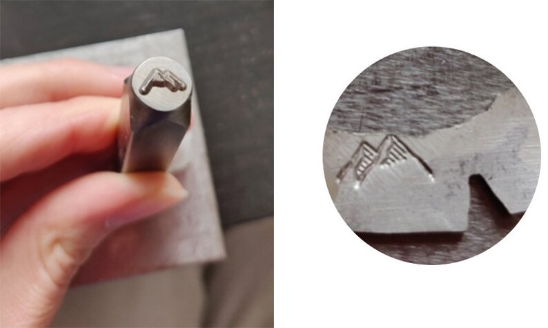 May include: Close-up of a metal stamp with a mountain range design. The stamp is used to create an impression on metal.