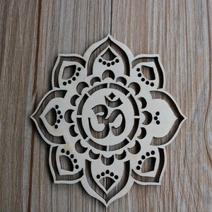 May include: A wooden mandala with a carved Om symbol in the center. The mandala is made of light brown wood and has a delicate, intricate design.