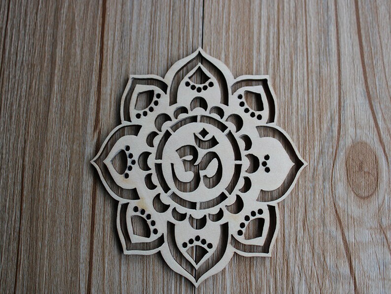 May include: A wooden mandala with a carved Om symbol in the center. The mandala is made of light brown wood and has a delicate, intricate design.