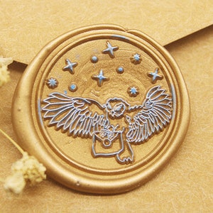 Puede incluir: Sello de cera dorado con un diseño detallado de un búho con las alas extendidas volando por un cielo estrellado.
