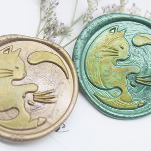 May include: Two wax seals with a cat design. One seal is gold with a green cat and the other is green with a gold cat.