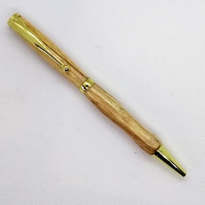 May include: A wooden pen with a gold-colored clip and tip. The pen is made of light brown wood with a natural grain pattern.