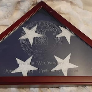 May include: Triangular wooden display case with a dark finish, showcasing a blue background with white stars and the emblem of the Air Force. The case includes the name "William W. Crawford" and dates.