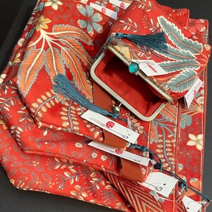 May include: A collection of red floral patterned accessories, including a clutch with a gold frame and teal stone clasp, a matching scarf, and other items. The set features teal tassels and tags.