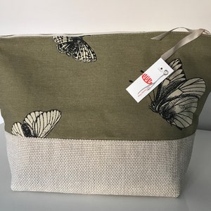May include: A green canvas zippered pouch with a beige bottom. The pouch has a black and white butterfly print and a white tag with the text "The Creative Yarn".