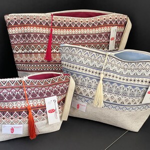 May include: Three zippered pouches with geometric patterns and tassels. The pouches are made of a woven fabric with a beige linen lining. The pouches are in different sizes and colours, including red, orange, blue, and white.