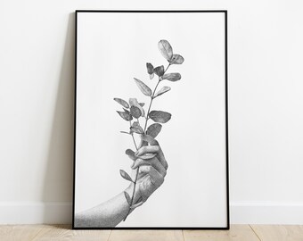 Pode incluir: Impressão artística a preto e branco com uma mão segurando um ramo de folhas. A obra de arte é uma ilustração detalhada em pontilhismo, emoldurada em preto, sobre um fundo branco. A impressão tem um tema botânico.