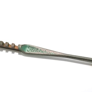 May include: A vintage glass cutter with a metal handle and a cutting head. The handle is a dark gray color with the word "Fletcher" printed on it in a faded green color. The cutting head has multiple small cutting wheels.