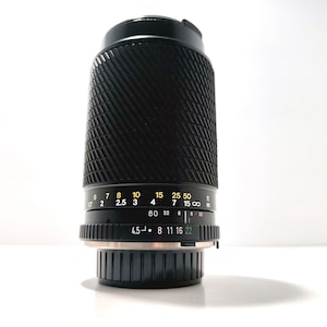 May include: A black camera lens with ribbed texture and a series of numbered markings in yellow and white. The lens has a metallic base and a black top. The numbers include 2, 2.5, 3, 4, 7, 15, 22, 50, and 80.