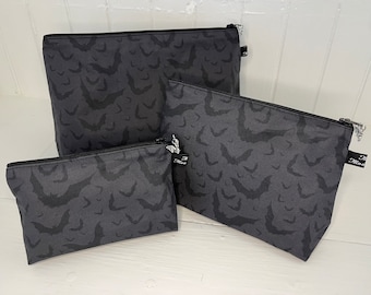May include: Three gray zippered pouches with a black bat pattern. The pouches are different sizes and are arranged in a row from largest to smallest.