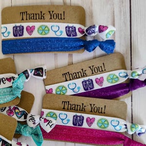 May include: Thank you tags with colorful elastic hair ties featuring medical symbols, hearts, and a stethoscope. The tags are brown with white text.