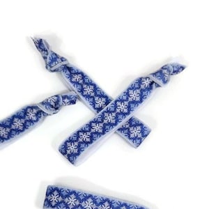 Könnte beinhalten: Drei blaue und weiße Gummibänder für Haare mit einem Schneeflockenmuster.