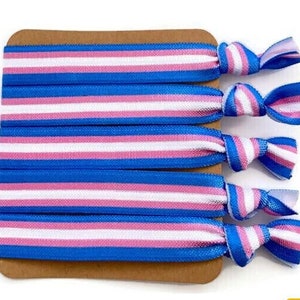 May include: A set of five blue, pink, and white striped hair ties on a brown card. The hair ties are tied in a knot.