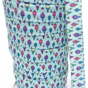 May include: A roll of turquoise blue elastic with a repeating pattern of ice cream cones and cherries. The elastic is wound around a cardboard spool.