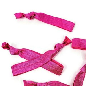 May include: Five pink elastic hair ties, each tied in a knot, are arranged on a white background.