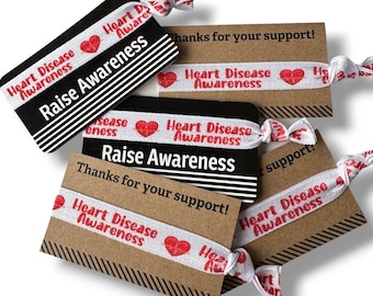 May include: A collection of heart disease awareness hair tie cards. The cards are black and brown with white and red text that reads "Heart Disease Awareness" and "Raise Awareness". The cards also say "Thanks for your support!"