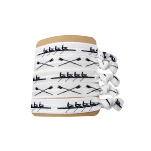 Puede incluir: Un conjunto de cinco gomas elásticas para el pelo blancas con un diseño de equipo de remo negro. Las gomas para el pelo están agrupadas y atadas con un nudo.