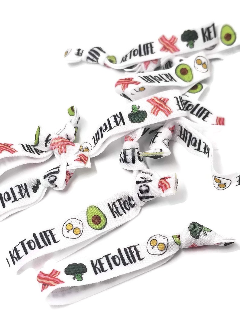 May include: White elastic hair ties with a keto-themed design. The hair ties feature images of avocado, bacon, eggs, and broccoli. The text "Keto Life" is printed on the hair ties.