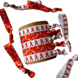 May include: A set of 6 white elastic hair ties with a red ribbon pattern. The hair ties are arranged in a circle around a brown cardboard backing.