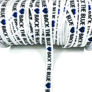 May include: White elastic ribbon with the text "Back the Blue" and blue hearts printed on it. The ribbon is rolled up on a spool.