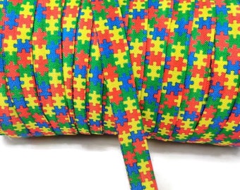 Może przedstawiać: Rolka kolorowej gumki z wzorem puzzli. Gumka jest czerwona, żółta, niebieska i zielona.