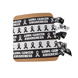 May include: Three black and white elastic hair ties with the text "Lung Cancer Awareness" and a silver ribbon design.