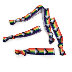 May include: Four rainbow-colored elastic hair ties with a geometric pattern of triangles. The hair ties are tied in knots and are arranged in a scattered pattern on a white background.