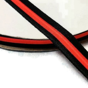 May include: Black and orange striped ribbon on a white spool. The ribbon is a woven fabric with a smooth texture.