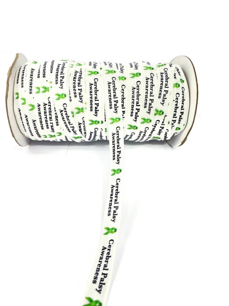 May include: A roll of white ribbon printed with the words "Cerebral Palsy Awareness" in black and green. The ribbon features green awareness ribbons. The roll is on a white background.