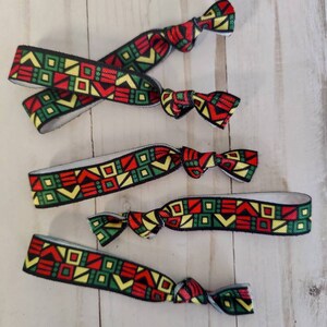 May include: Five colorful hair ties with a geometric pattern in red, yellow, green, and black. The hair ties are made of elastic material and are tied in a knot.