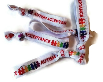 May include: White elastic hair ties with the text "Autism Acceptance" and a rainbow puzzle piece symbol.