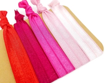 May include: Five colorful hair ties in shades of red, pink, and white. The hair ties are arranged in a gradient from red to white.