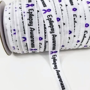 Op de afbeelding: Een rol wit elastisch lint met een paars lint en de tekst "Epilepsy Awareness" die op elke lus wordt herhaald.