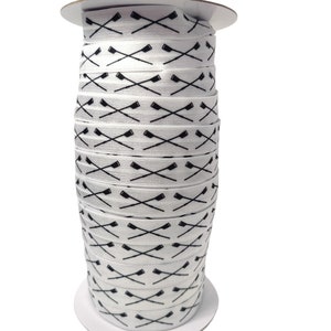 May include: A spool of white elastic ribbon with a black repeated pattern of crossed oars.