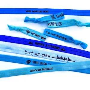 May include: A collection of blue and light blue elastic hair ties with various text printed on them, including "Your wording here", "Forever You", "Mount 3 Fitness", "M.T. Crew", "Style Salon", and "Alex's 8th Birthday!"