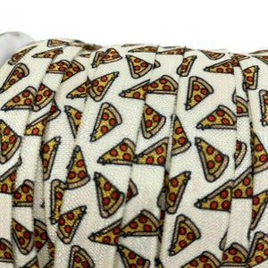 Puede incluir: Una banda elástica blanca con un patrón repetido de rebanadas de pizza. Las rebanadas de pizza son amarillas, marrones y rojas con pepperoni.