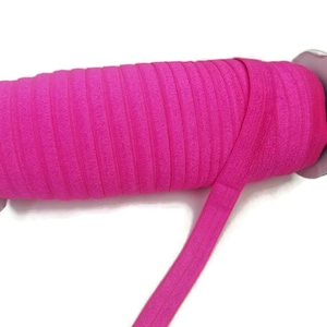 May include: A roll of bright pink elastic, folded and displayed on a white background. The elastic is approximately 1/2 inch wide.