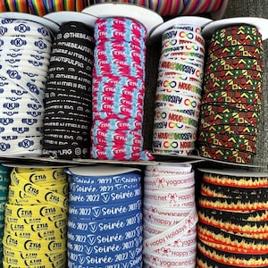 Peut inclure: Une collection d'&eacute;lastiques &agrave; cheveux color&eacute;s avec diff&eacute;rents motifs et textes. Les motifs comprennent des rayures arc-en-ciel, un motif tie-dye, un motif noir et blanc avec le texte "Neurodiversity", un motif noir et vert avec des formes g&eacute;om&eacute;triques, un motif jaune et noir avec le texte "Ziya Active", un motif bleu et blanc avec le texte "Soir&eacute;e 2022", un motif blanc et rouge avec le texte "Happy Holidays", et un motif noir et orange avec des flammes.