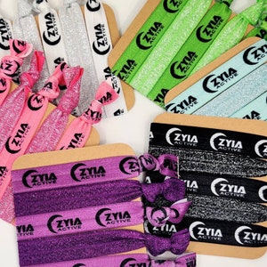 May include: Assortment of colorful hair ties with glitter and the text "ZYIA ACTIVE" printed on them. The hair ties are arranged on brown cardboard cards.