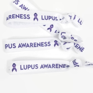 Puede incluir: Tres gomas elásticas para el pelo blancas con el texto "Lupus Awareness" y una cinta morada impresa.