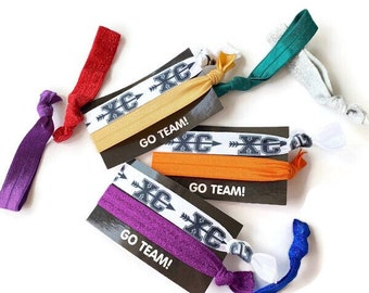 May include: Set of six hair ties with a white and black patterned band that says "XC" and "GO TEAM!" The hair ties are in various colors: red, yellow, green, silver, purple, and blue.