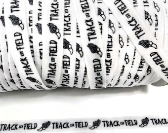 May include: White elastic ribbon with black print that reads "TRACK & FIELD" and a running shoe icon. The ribbon is rolled up.