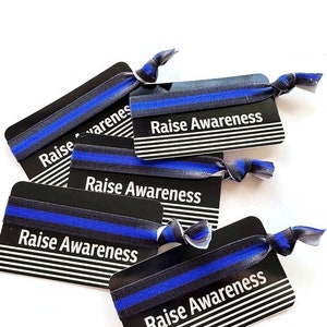 May include: Five black and white cards with a blue and black striped elastic hair tie on each card. The cards have the text "Raise Awareness" printed on them.