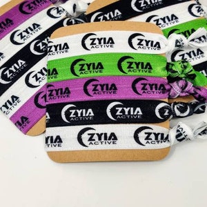 May include: A set of four hair ties with the logo "ZYIA ACTIVE" printed on them. The hair ties are in black, white, green, and purple.